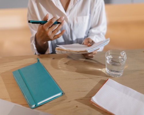 A person neatly organizing notes and drinking a glass of water at a bright local cafe table